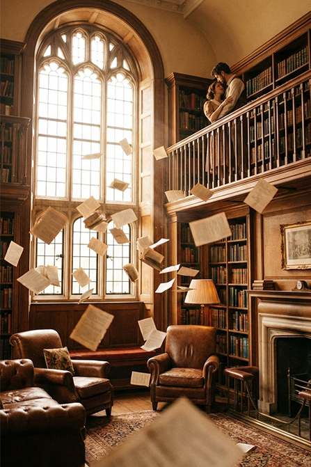 Bibliotecă elegantă luminată cald, cu pagini scrise care plutesc în aer, simbolizând poveștile care prind viață și emoția de a-ți spune propria poveste.