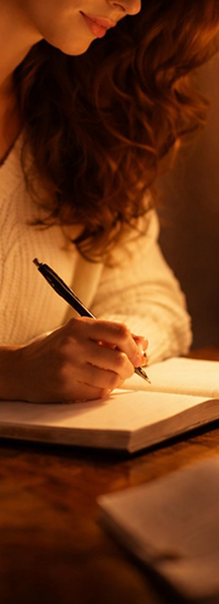 Femeie care scrie într-un jurnal la birou, într-o atmosferă caldă, simbol al procesului de autocunoaștere din Culorile Iubirii.